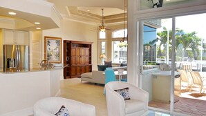 A spacious living area with a large window, a ceiling fan, and a modern kitchen with a refrigerator. - Pet-friendly Waterfront Home With Heated Pool and spa (Marco Island)