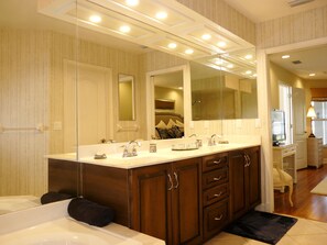A bathroom with a large mirror, a double sink, and wooden cabinets. - 910 Olive Court (Marco Island)