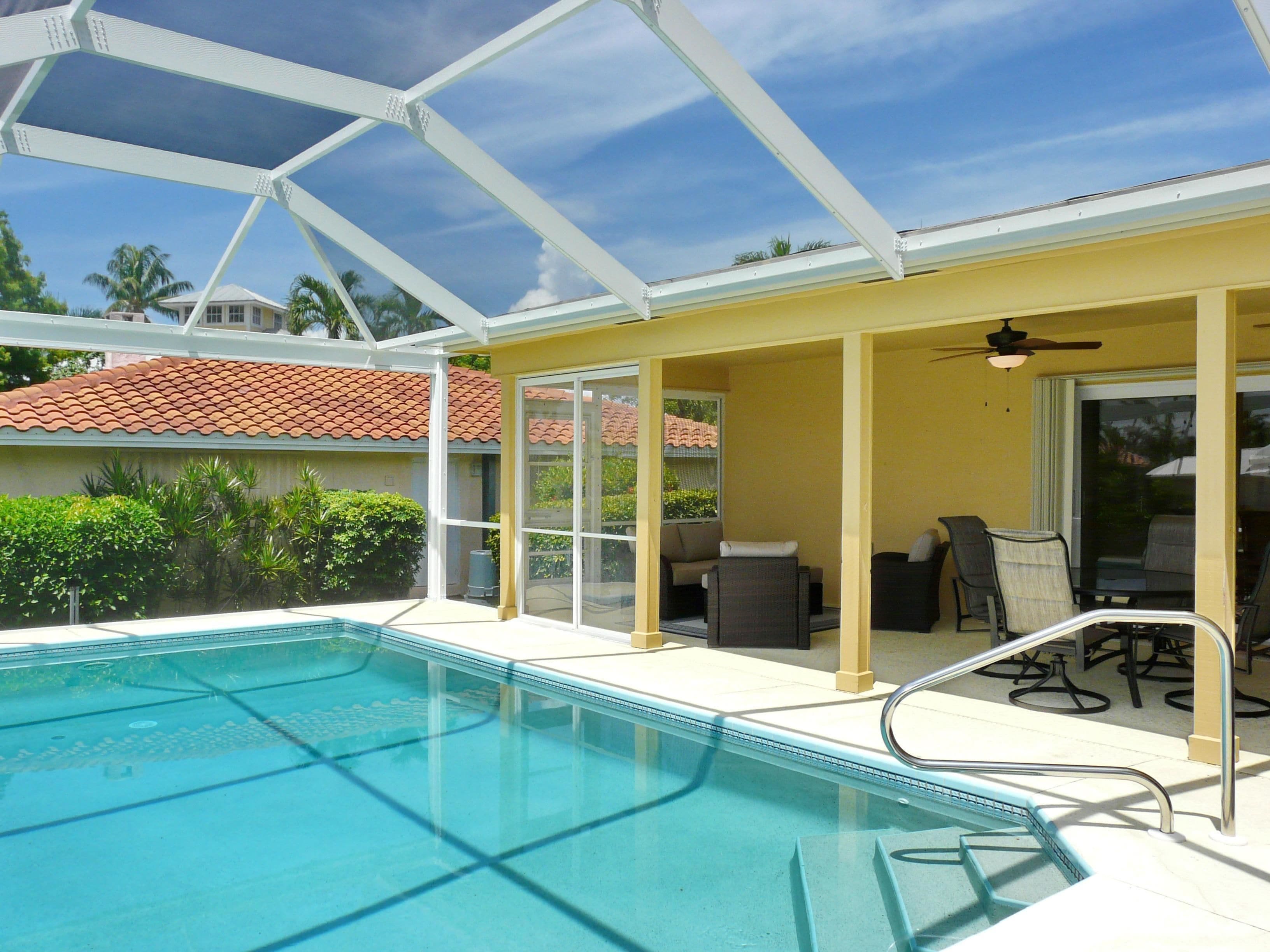 A covered pool area with a glass enclosure, a ceiling fan, and a patio with outdoor furniture.