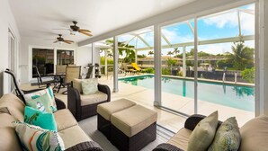 A sunlit room with a pool view, wicker furniture, ceiling fans, and a patio area. - Idyllic Waterfront Home With Pool and Western Exposure (Marco Island)