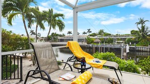 A balcony with a chair, a table, and a yellow towel. - Idyllic Waterfront Home With Pool and Western Exposure (Marco Island)