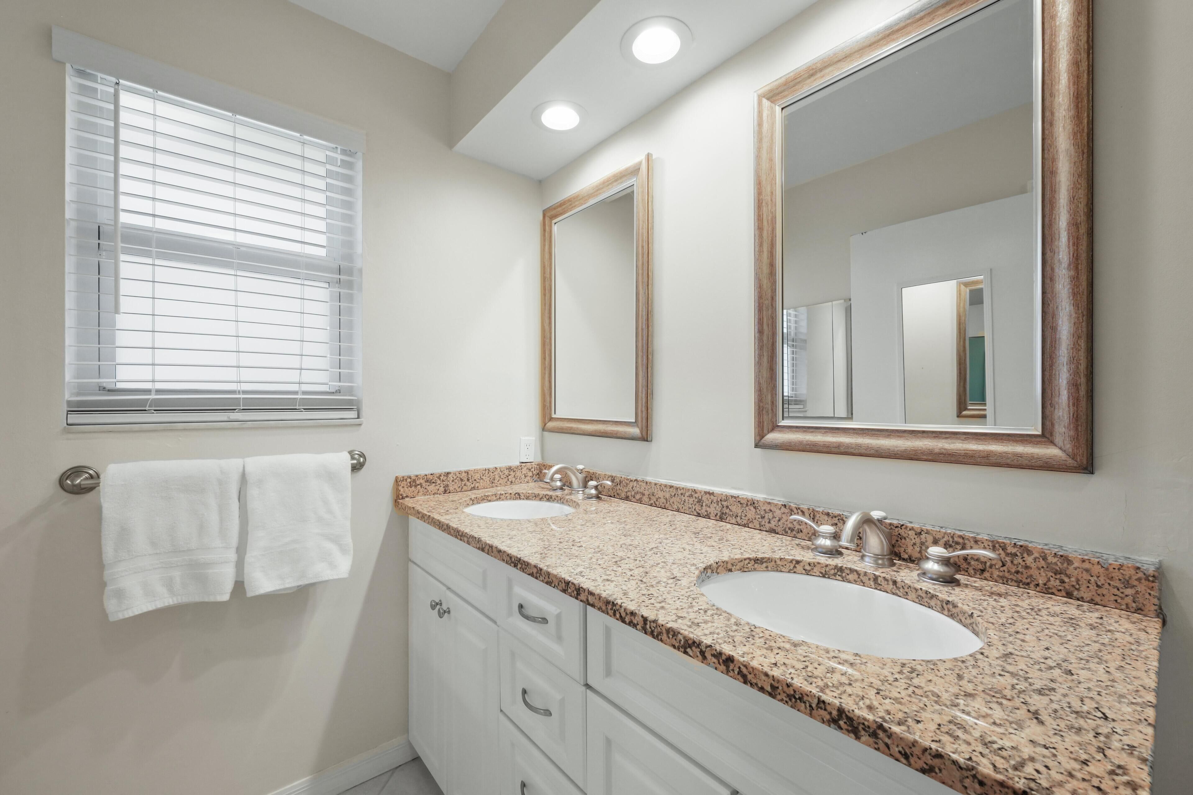 A bathroom with two sinks, a large mirror, and a window with blinds.