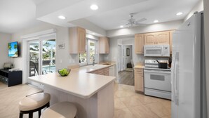 A modern kitchen with a central island, white appliances, and wooden cabinets. - Idyllic Waterfront Home With Pool and Western Exposure (Marco Island)
