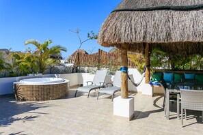 Una terraza en la azotea con jacuzzi, sillones de descanso, una mesa de comedor y un paraguas de paja.