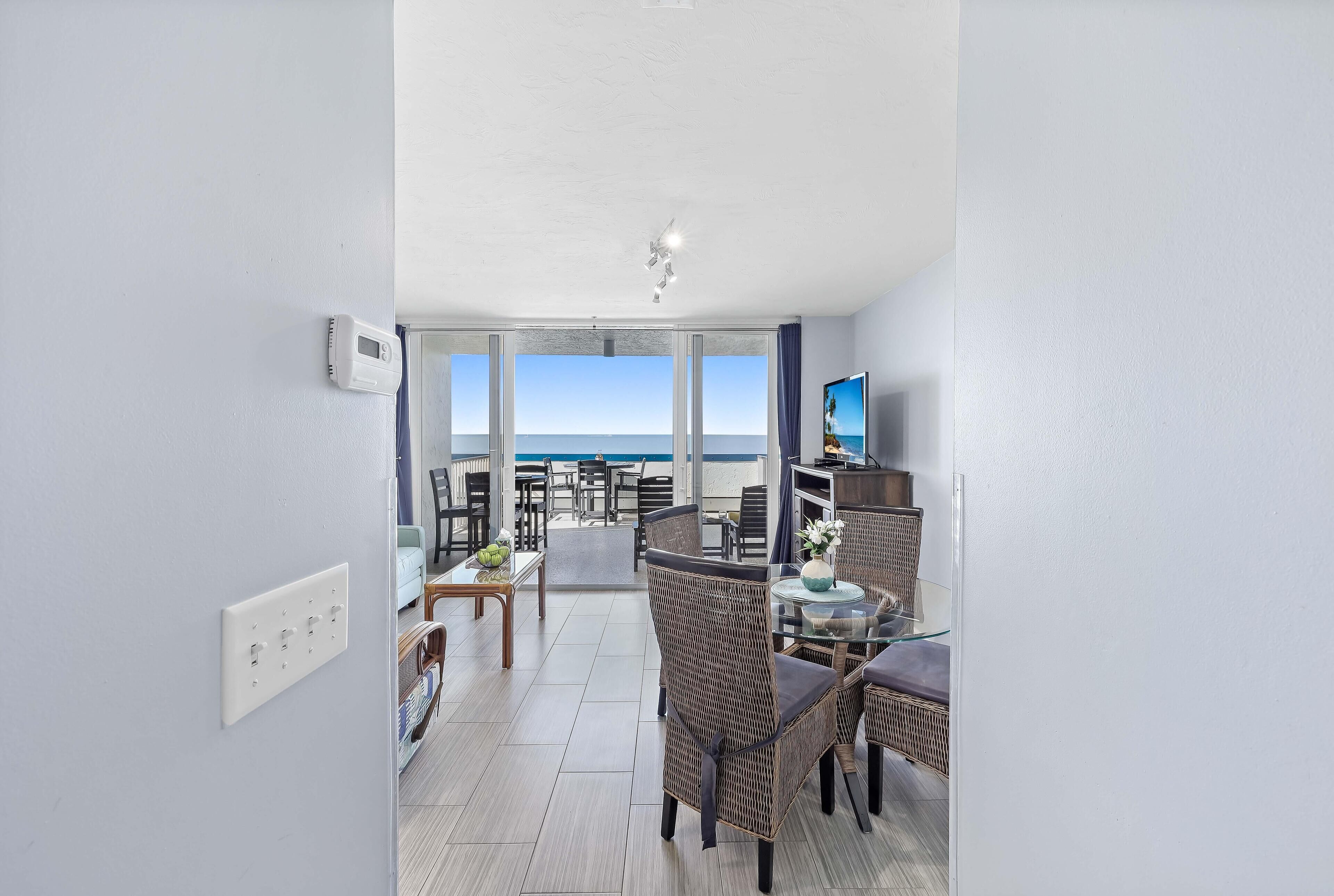 A modern hotel room with a balcony, furnished with wicker chairs and a glass table, overlooking the sea.