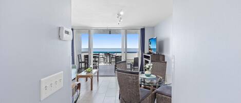 A modern hotel room with a balcony, furnished with wicker chairs and a glass table, overlooking the sea.