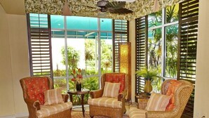 A room with wicker furniture, large windows, and a ceiling fan. - Unmatched Beachfront Condo With Roomy Balcony and Pool (Marco Island)