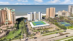 A coastal hotel complex with multiple high-rise buildings, a central tennis court, and a beach view. - Unmatched Beachfront Condo With Roomy Balcony and Pool (Marco Island)