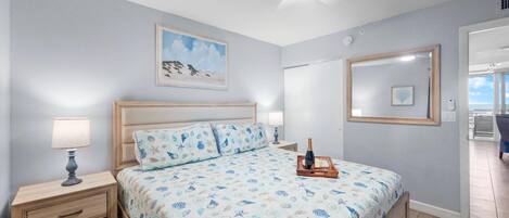Un dormitorio con cama, mesitas de noche, ventilador de techo, un cuadro enmarcado y vistas al exterior.