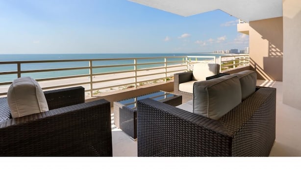 A balcony with wicker furniture overlooking a beach. - Beachfront Condo With 180-degree Views and Pool (Marco Island)