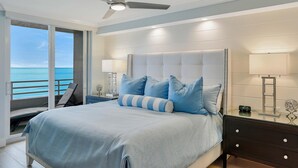 A bedroom with a large bed, a ceiling fan, a nightstand with a lamp, and a view of the ocean. - Beachfront Condo With 180-degree Views and Pool (Marco Island)
