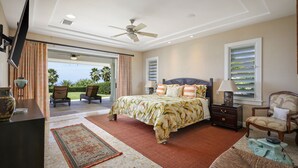 Ein Schlafzimmer mit Bett, Fernseher, Deckenventilator und Blick ins Freie.