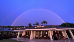 Ein Haus mit überdachter Terrasse und einem großen, bogenförmigen Regenbogen am Himmel.