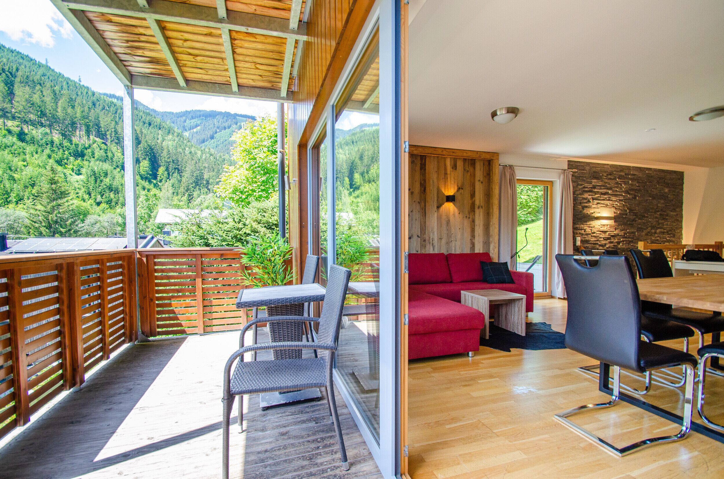 Een modern interieur met een houten terras, een rode bank en een eethoek met een accentmuur van steen.