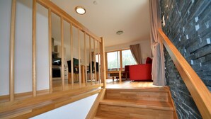 A wooden staircase leading to a living area with a red sofa, a dining table, and a kitchen in the background. - Schmitten Finest Apartment - SKYBLUE (Zell am See)