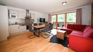 A modern kitchen with a dining area, a red sofa, and a large sliding glass door to the outdoors. - Schmitten Finest Apartment - SKYBLUE (Zell am See)