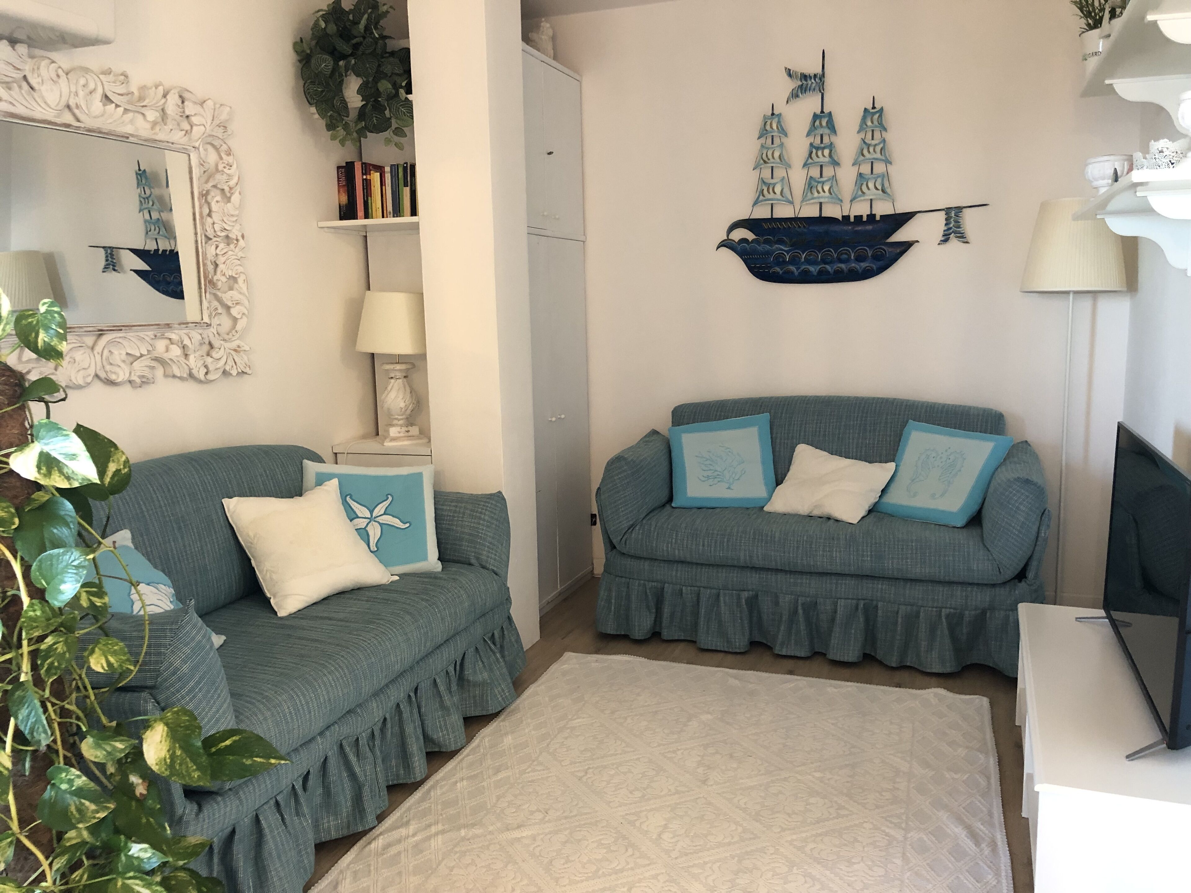 Una sala de estar con dos sofás, un tapete estampado, una estantería, un mural decorativo de un barco y una planta en maceta.