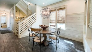A dining area with a round table, four chairs, a chandelier, and a staircase in the background.