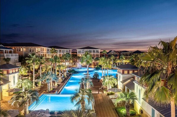 Relax by the resort's central pool surrounded by palm trees and lounge areas, with stunning views from the balconies of the multi-story buildings.