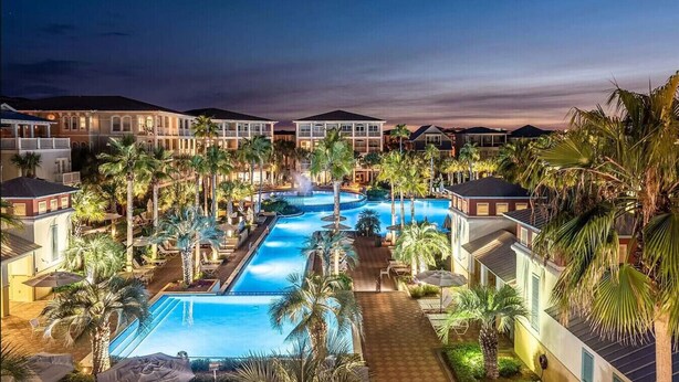 A resort with a large swimming pool surrounded by palm trees and multiple hotel buildings.