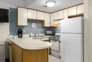 Cocina compacta con microondas, estufa y refrigerador. Hay un reloj en la pared y una cafetera en la encimera.