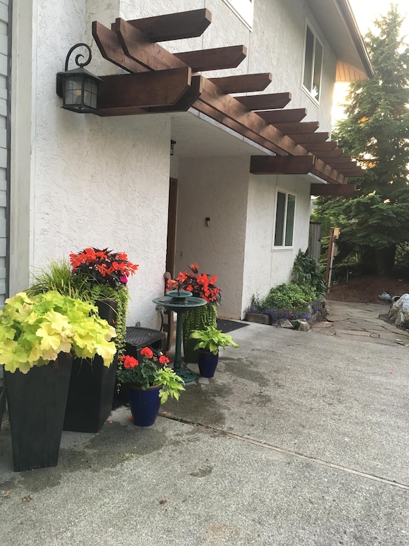 Un edificio con fachada blanca, una pérgola de madera y macetas con flores rojas y amarillas.