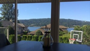 Un comedor con mesa y sillas, un aro de baloncesto y vistas a un lago y casas.