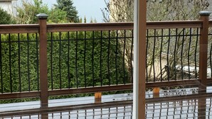 Una terraza de madera con barandilla de metal que da a un lago y colinas boscosas.
