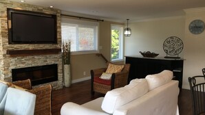 Una sala de estar con chimenea, un televisor de pantalla plana montado en la pared, muebles de mimbre y un reloj en la pared.