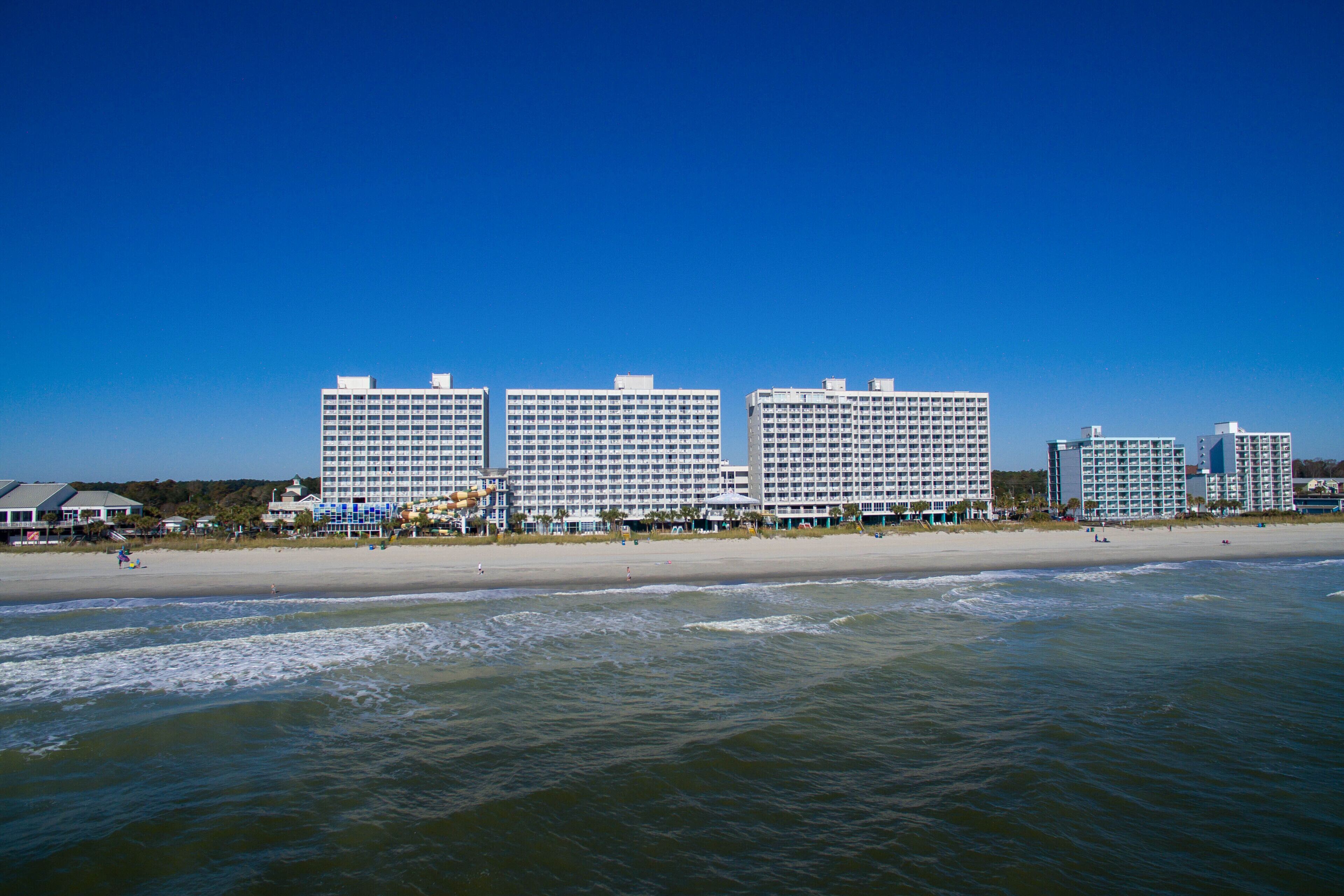 A beachfront hotel with multiple high-rise buildings, a sandy beach, and ocean waves.