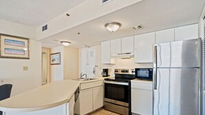 A modern kitchen with white cabinets, stainless steel appliances, and a tiled floor.