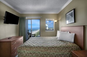 A hotel room with a bed, a dresser, a TV, a balcony with a chair, and a view of the ocean.