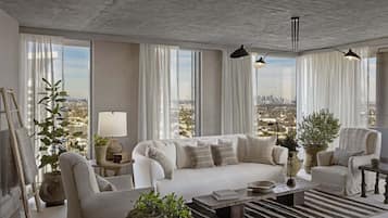 A modern living room with a white sofa, armchairs, and a coffee table. There are large windows with sheer curtains, a view of a cityscape, and a potted plant.