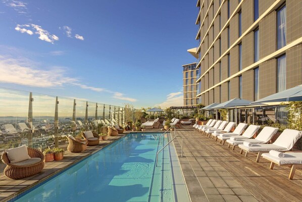 Una piscina en la azotea con sillones de descanso y vistas de la ciudad.