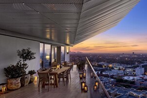 Una terraza en la azotea con zona de comedor, plantas en macetas y vistas a la ciudad al atardecer.