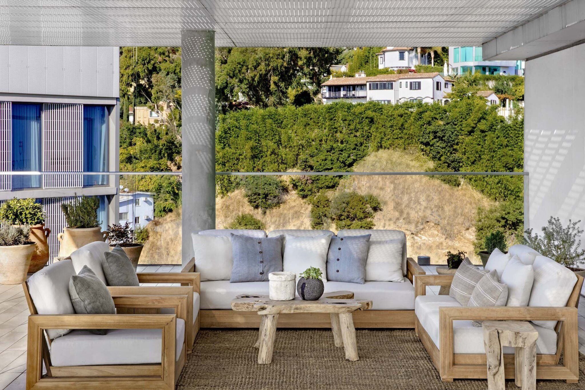 A modern outdoor seating area with a sofa and chairs, a wooden coffee table, and potted plants.