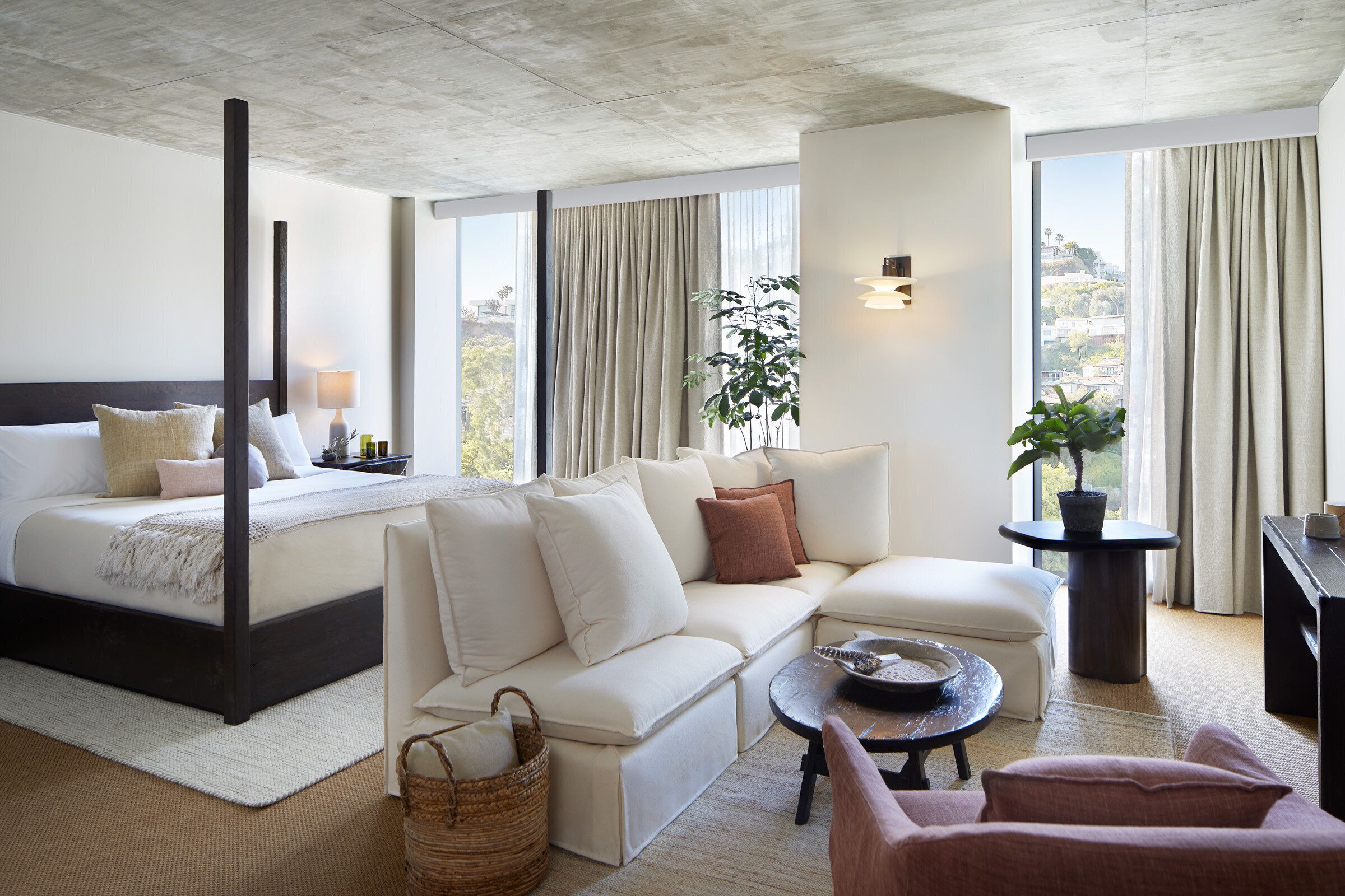 A modern hotel room with a large bed, a sofa, a coffee table, and a view of the city.