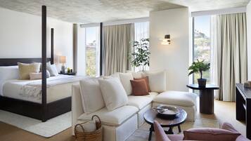 A modern hotel room with a large bed, a sofa, a coffee table, and a view of the city.