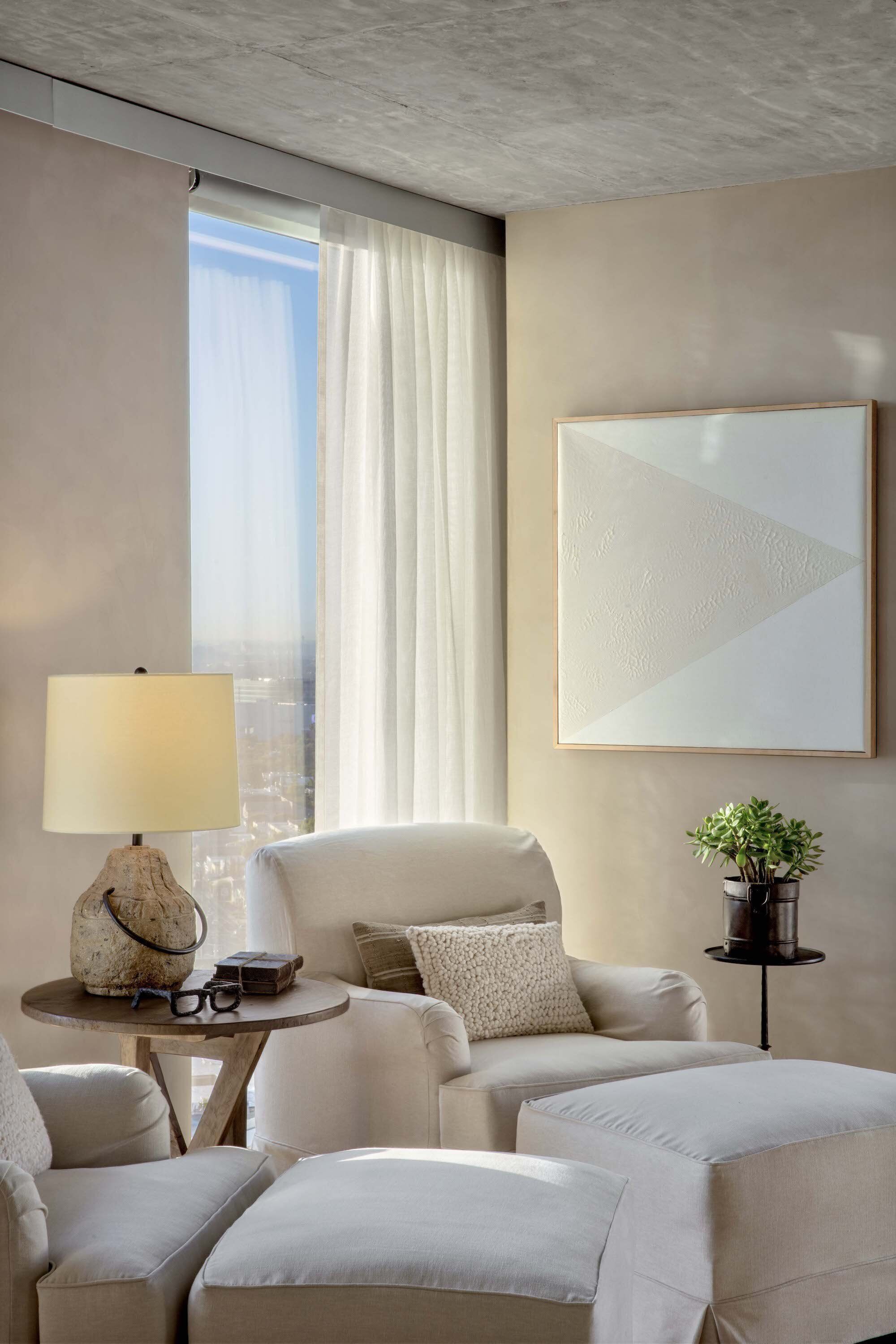 Een moderne hotelkamer met een groot raam, een bank, een klein tafeltje met een lamp en een lijst met een kunstwerk aan de muur.