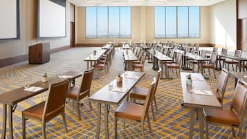 Una sala de conferencias con varias mesas y sillas, amplias ventanas que dan a vistas de la ciudad y un atril.