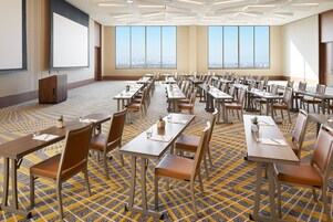 Una sala de conferencias con varias mesas y sillas, amplias ventanas que dan a vistas de la ciudad y un atril.