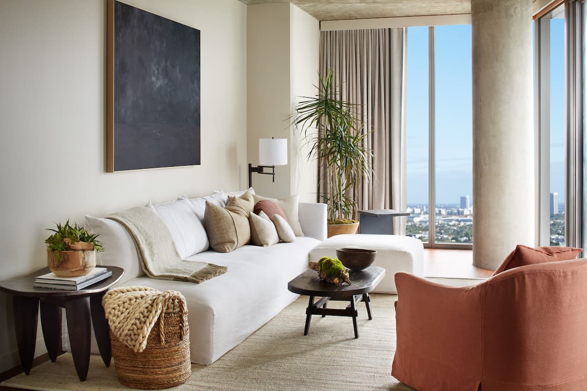 Un salon moderne avec un canapé blanc, une petite table d’appoint, une table basse et une vue sur la ville grâce à de grandes fenêtres.