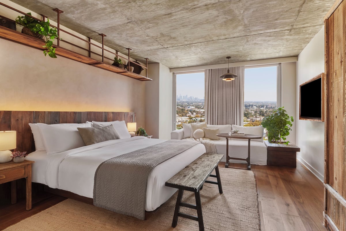Une chambre d’hôtel moderne avec un grand lit, un banc en bois, une petite table et un téléviseur.