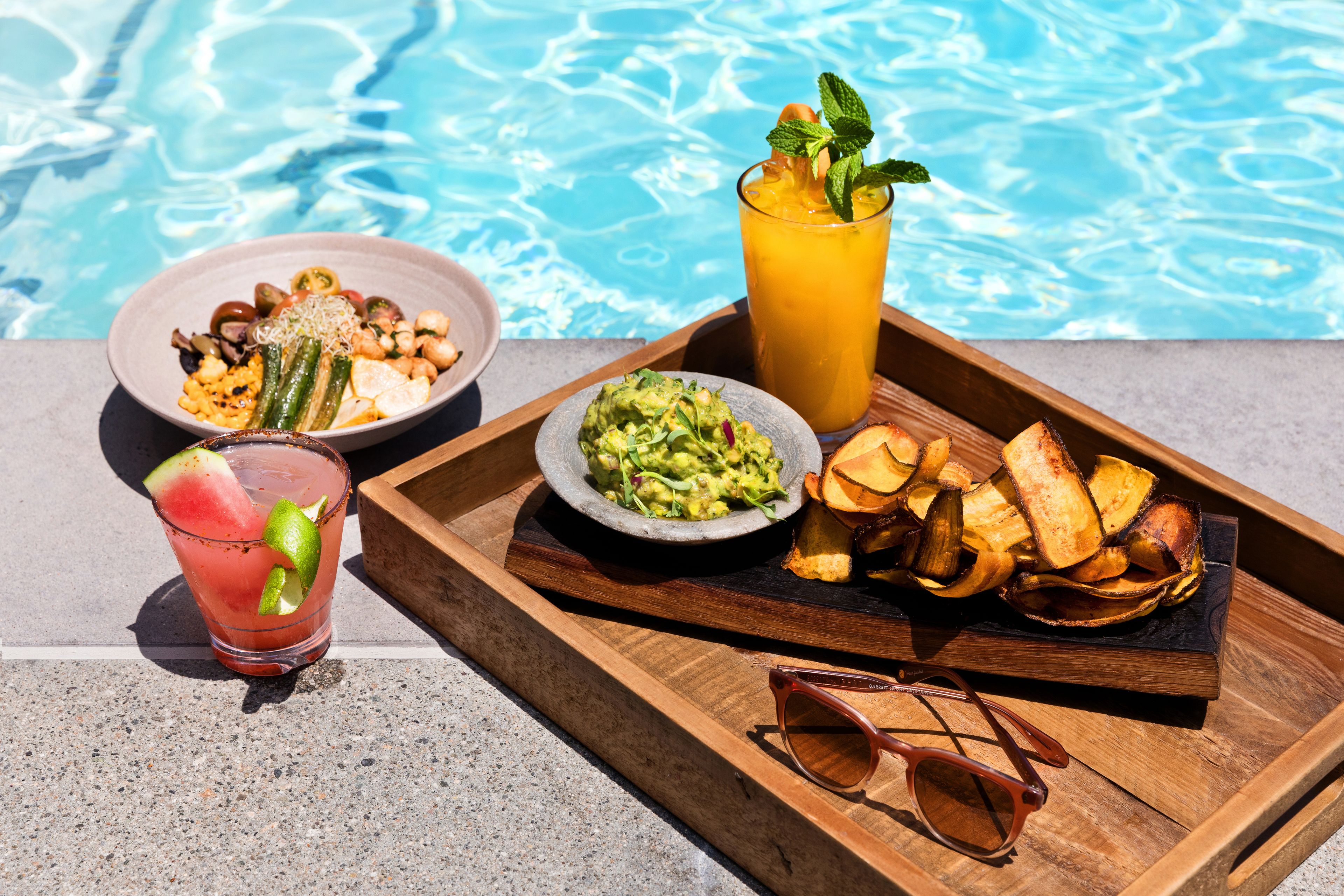 Una bandeja con comida y bebidas junto a una piscina.