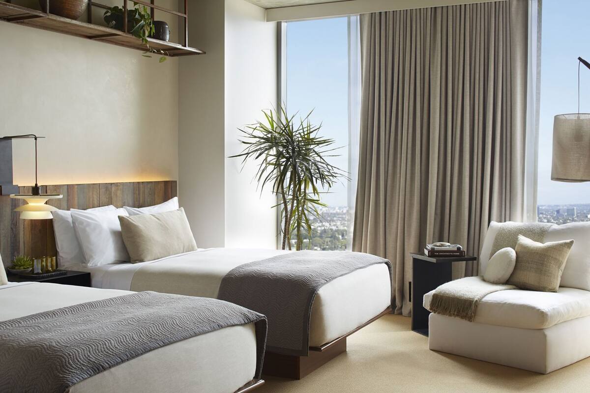 Une chambre d’hôtel avec deux lits, un canapé, une plante et une vue sur la ville.