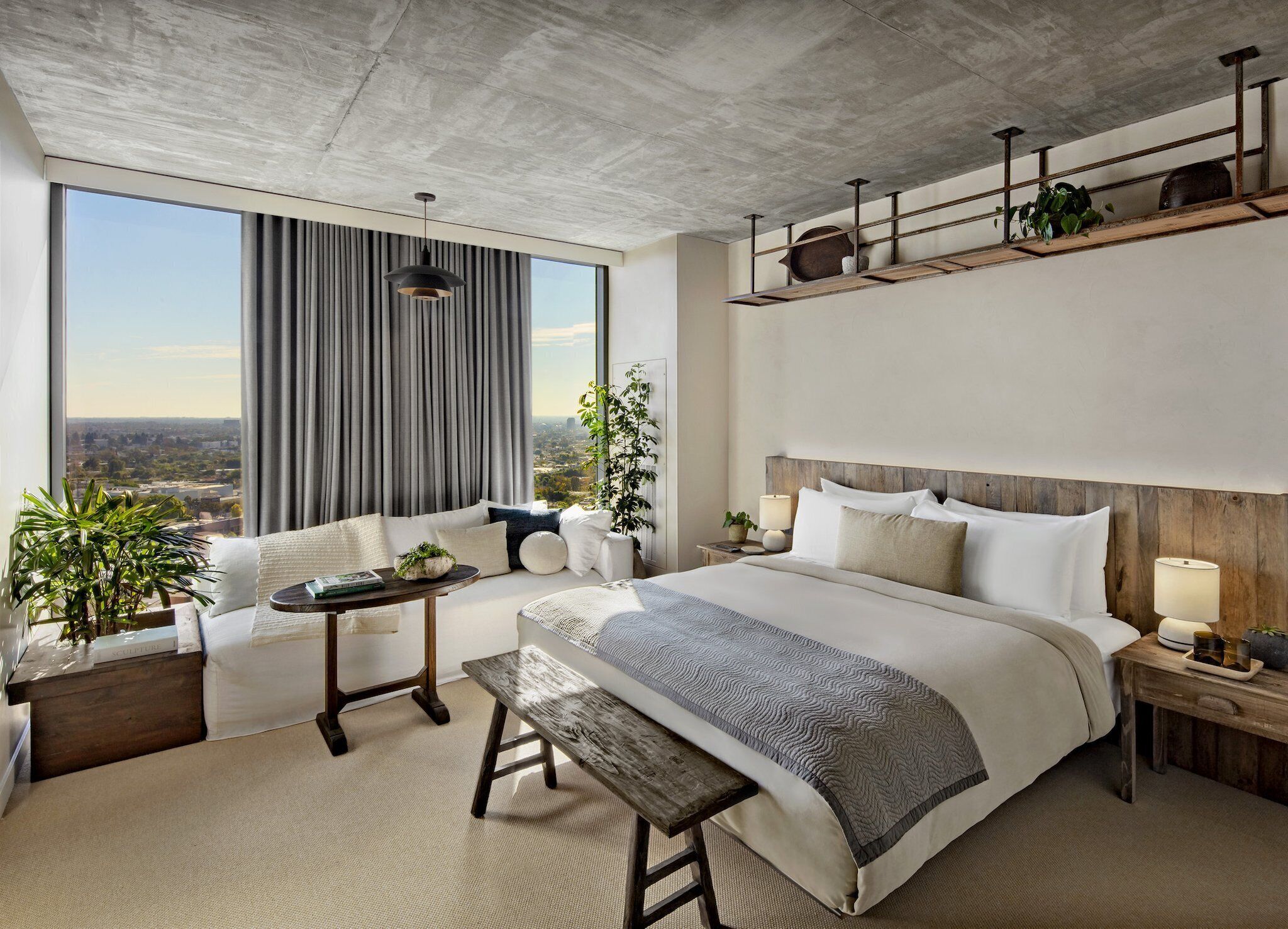 Une chambre d’hôtel moderne dotée d’un grand lit, d’un coin salon, d’une vue sur la ville et d’un balcon agrémenté de plantes.