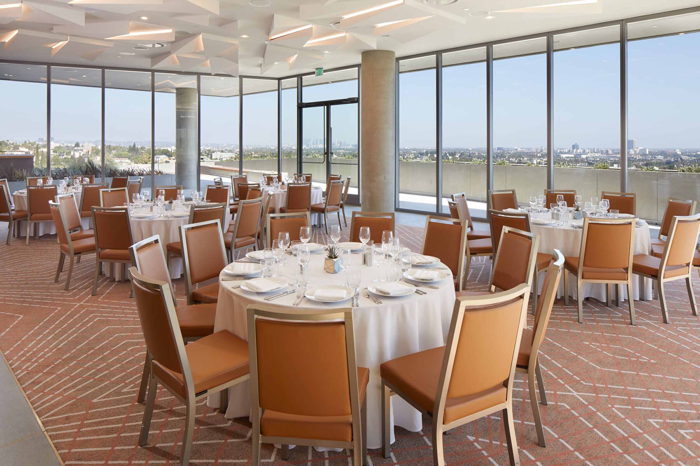 Un espace de restauration aménagé sur le toit, avec des tables rondes disposées pour accueillir les clients, de grandes fenêtres offrant une vue sur la ville et un sol en briques.