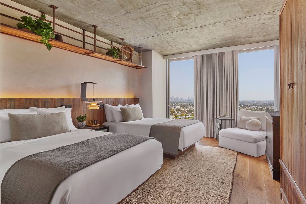 Une chambre d’hôtel moderne avec deux lits, un canapé, une grande fenêtre donnant sur la ville et un plafond en bois.