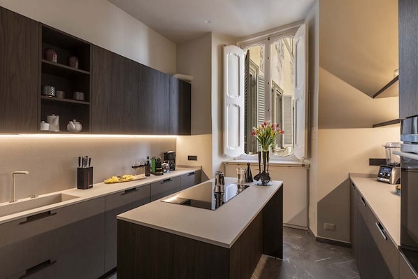 A modern kitchen with dark cabinetry, a central island, and a window with shutters.