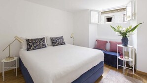 Un dormitorio con una cama grande, lámparas de noche, una mesita, un banco y una planta en maceta.
